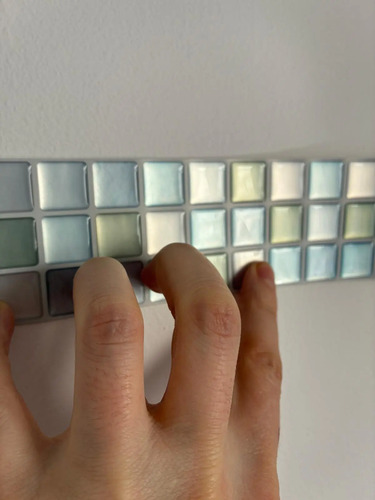 Detalle de placa mosaico 3D autoadhesiva celeste con cuadrados en relieve, tocada con la mano