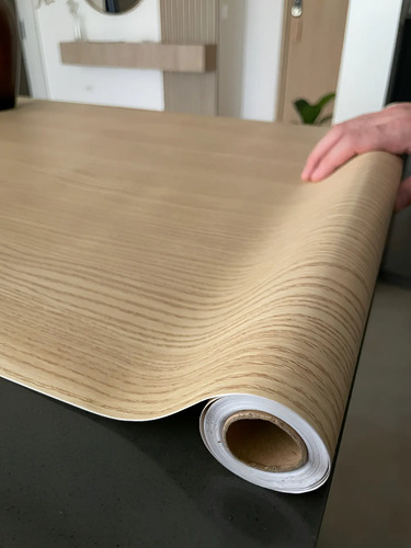 Rollo de papel autoadhesivo texturizado imitación madera marrón claro siendo desenrollado.