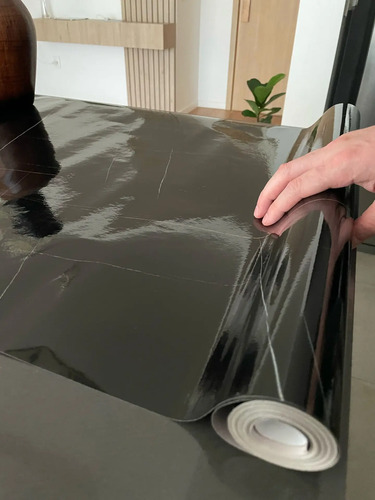 Papel autoadhesivo mármol gris siendo desenrollado, mostrando su textura y acabado impermeable.