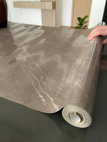 Papel mármol autoadhesivo gris con vetas siendo desplegado desde su rollo