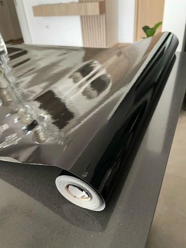 Rollo de papel adhesivo negro liso siendo desenrollado, mostrando la superficie brillante y el tubo de cartón.