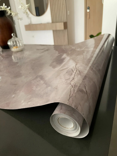 Rollo de papel adhesivo mármol gris con vetas, parcialmente desenrollado sobre superficie oscura