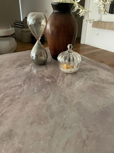 Papel adhesivo mármol gris aplicado en superficie de mesa, con decoración de reloj de arena y jarrón cerámico.
