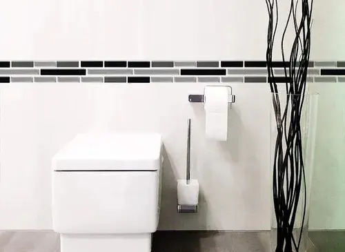Guarda autoadhesiva mosaico 3D instalada en pared de baño junto a inodoro blanco