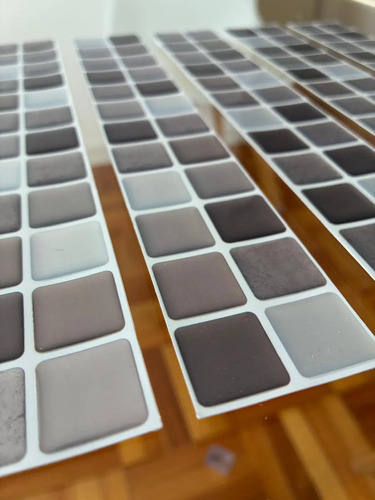 Guardas adhesivas 3D con patrón de mosaico en tonos grises y blancos, vistas en ángulo sobre madera.