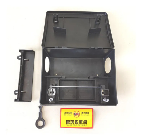Caja cebadera abierta: compartimento interior con bandeja de cebo y varilla metálica, dos entradas laterales, llave, soporte de pared y etiqueta de advertencia