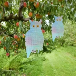 Búho ahuyentador de pájaros reflectante colgado en un árbol frutal. Dispositivo ecológico para repeler aves.